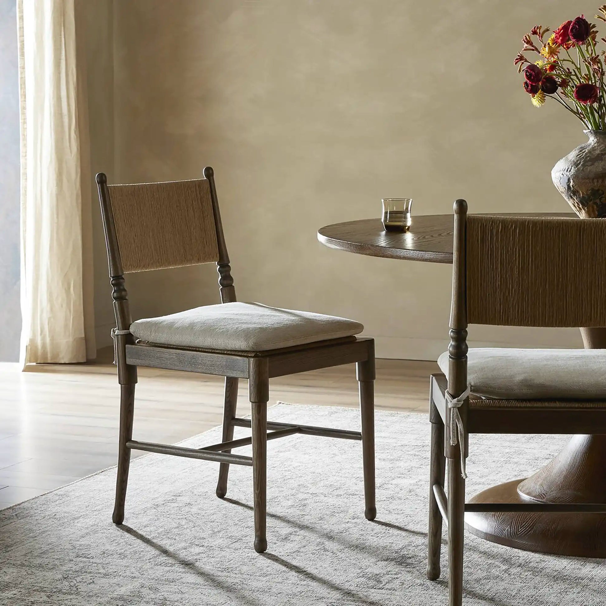 Four wooden chairs around a round marble dining table, with cushions, in a bright room