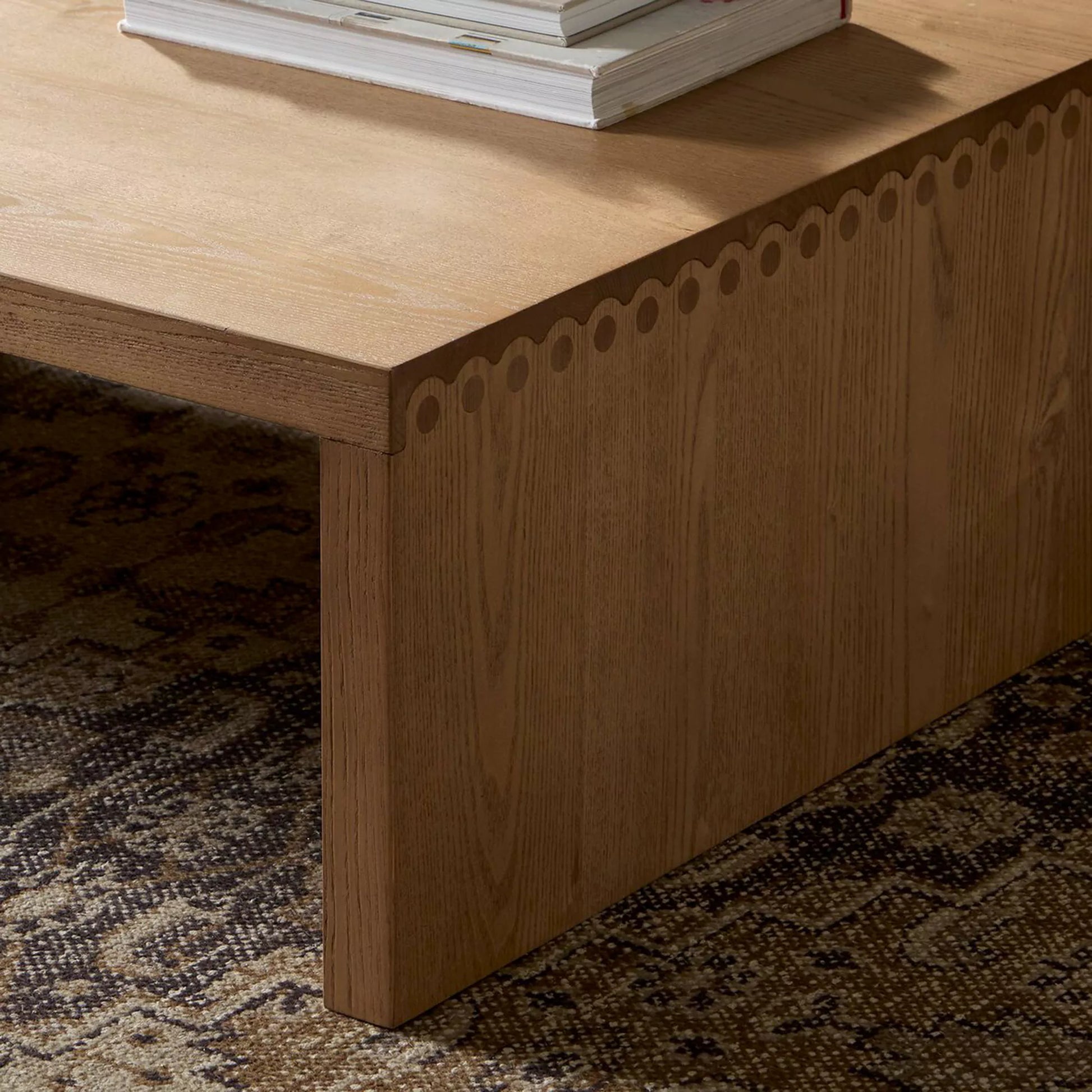 Close-up of a wooden corner table with patterned edge trim, on a carpeted floor